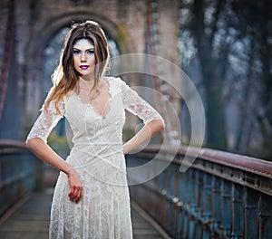 Lovely young lady wearing elegant white dress enjoying the beams of celestial light and snowflakes falling on her face