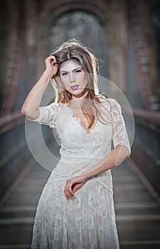 Lovely young lady wearing elegant white dress enjoying the beams of celestial light and snowflakes falling on her face