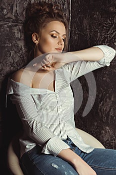 Lovely young model sitting on a chair in striped and torn jeans