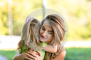 Lovely young mom and daughter in warm sunny summer day. Happy family mother and child little daughter hugging and