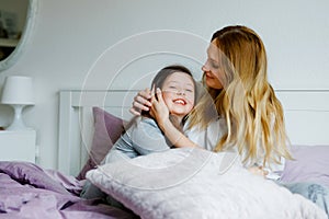 Lovely young mother and cute school kid girl cuddling together in bed in morning. Happy family of young single woman and