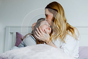 Lovely young mother and cute school kid girl cuddling together in bed in morning. Happy family of young single woman and