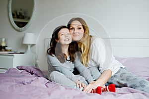 Lovely young mother and cute school kid girl cuddling together in bed in morning. Happy family of young single woman and