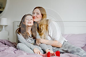 Lovely young mother and cute school kid girl cuddling together in bed in morning. Happy family of young single woman and