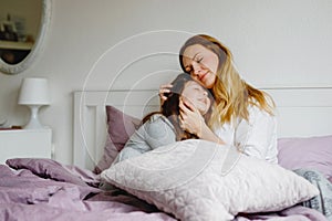 Lovely young mother and cute school kid girl cuddling together in bed in morning. Happy family of young single woman and