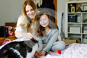 Lovely young mother and cute school kid girl cuddling together with cat in bed in morning. Happy family of young single