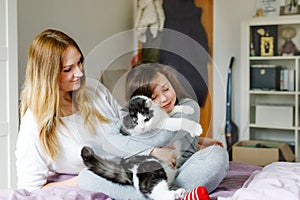 Lovely young mother and cute school kid girl cuddling together with cat in bed in morning. Happy family of young single