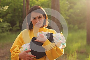 A lovely young mother with straight brown hair and in a yellow sweatshirt holds a small child in her arms in the forest in the