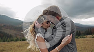 Lovely young newlyweds bride and groom embracing, making a kiss on mountain slope, wedding couple
