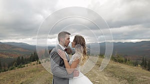 Lovely young newlyweds bride groom walking on mountain slope, making a kiss, wedding couple family