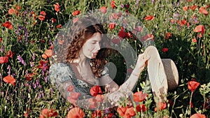 Lovely young romantic woman in hat falling in a poppy field