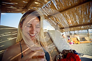 Lovely young woman drinking beer at beach, sitting on sunbed. Summertime vacation. Holiday, fun, lesiure, lifestyle concept