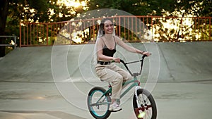 Lovely young woman riding bmx bike in the sunlight outdoor skatepark. Active people. Pretty girl with dreadlocks freerly