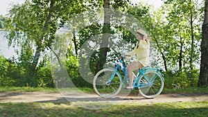 Lovely young woman in summer hat leisurely riding blue bicycle