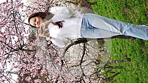 Lovely young woman taking photo of blooming pink and white garden Petrin in Prague, spring time in Europe