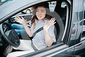 Lovely young woman is troubled with results of driving lesson. Attractive confused woman shrugs up or makes a helpless