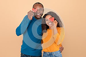 Lovers blinded by their big love. Black couple in love holding red heart-shaped cards over eyes and smiling