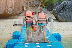 Lovers couple holding hands while walking on plastic pontoon walk way floating in the sea