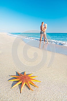 Lovers couple at sandy sea beach with big red starfish