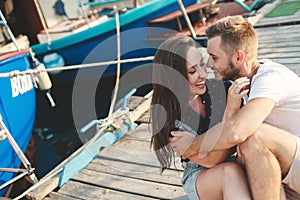 Lovers, guy and girl, are sitting on a wooden pier, holding hands and laughing