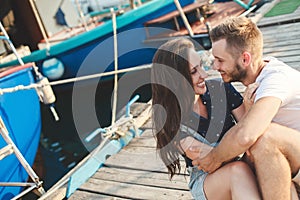 Lovers, guy and girl, are sitting on a wooden pier, holding hands and laughing