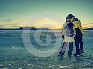 Lovers hold each other stay on ice in frozen lagoon and watch sun