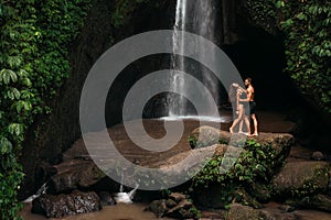 Lovers at the waterfall. Couple admiring a beautiful waterfall in Indonesia. Couple on vacation in Bali. Honeymoon trip.