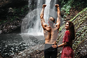 Lovers at the waterfall, rear view. Couple admiring a beautiful waterfall in Indonesia. Couple on vacation in Bali. Honeymoon trip