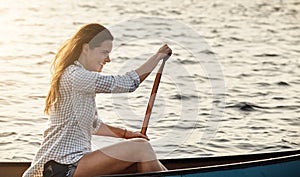 She loves the feeling rowing gives her. a beautiful young woman rowing a boat out on the lake.