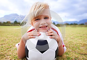 She loves the game. A young soccer player lying on the grass while holding a ball.