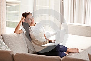 She loves her relaxed weekends. an attractive young woman relaxing on the couch with her laptop.