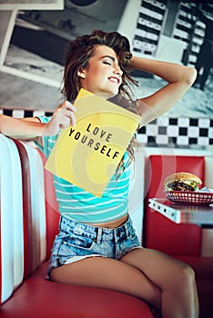 She loves herself. an attractive young woman holding up a sign in a retro diner.
