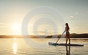 She loves the peace paddling gives her. an attractive young woman paddle boarding on a lake.