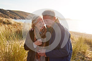 Loving Active Senior Couple Arm In Arm Walking Through Sand Dunes