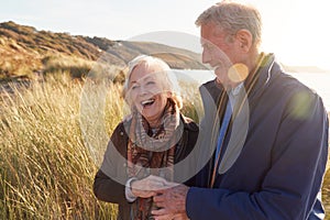 Loving Active Senior Couple Arm In Arm Walking Through Sand Dunes