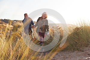 Loving Active Senior Couple Holding Hands As They Walk Through Sand Dunes