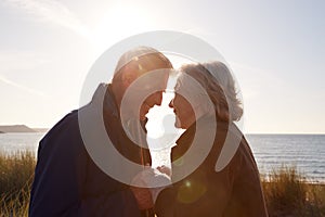 Loving Active Senior Couple Holding Hands As They Walk Through Sand Dunes Against Flaring Sun