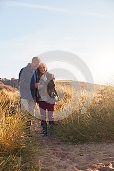 Loving Active Senior Couple Hugging As They Walk Through Sand Dunes