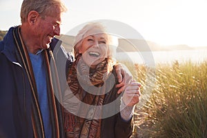 Loving Active Senior Couple Hugging As They Walk Through Sand Dunes