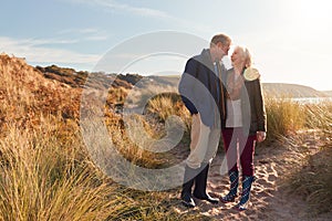 Loving Active Senior Couple Hugging As They Walk Through Sand Dunes