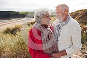 Loving Active Senior Couple Standing And Hugging On Walk In Sand Dunes On Winter Beach Vacation