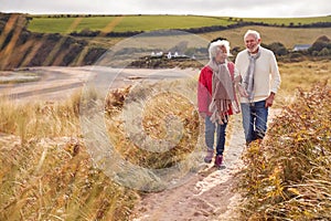 Loving Active Senior Couple Walking Arm In Arm Through Sand Dunes On Winter Beach Vacation