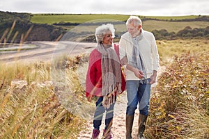 Loving Active Senior Couple Walking Arm In Arm Through Sand Dunes On Winter Beach Vacation