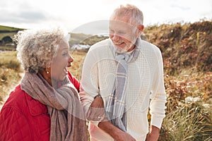 Loving Active Senior Couple Walking Arm In Arm Through Sand Dunes On Winter Beach Vacation