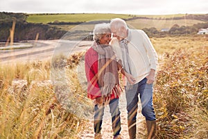 Loving Active Senior Couple Walking Arm In Arm Through Sand Dunes On Winter Beach Vacation