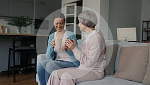 Loving adult daughter giving cup of tea to her old mother with mental disorder