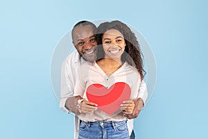 Loving african american couple celebrating their love, black middle aged man and young woman holding big red heart