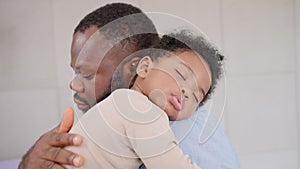 Loving African American dad embracing baby and baby girl sleeping on stepfather shoulder. Happy family with pleasure spending time