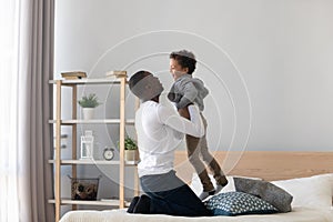Loving African American father playing with little son in bedroom