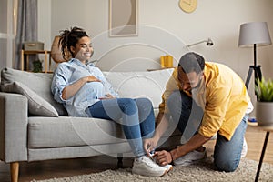 Loving African American Husband Helping Pregnant Wife Lacing Shoes Indoors